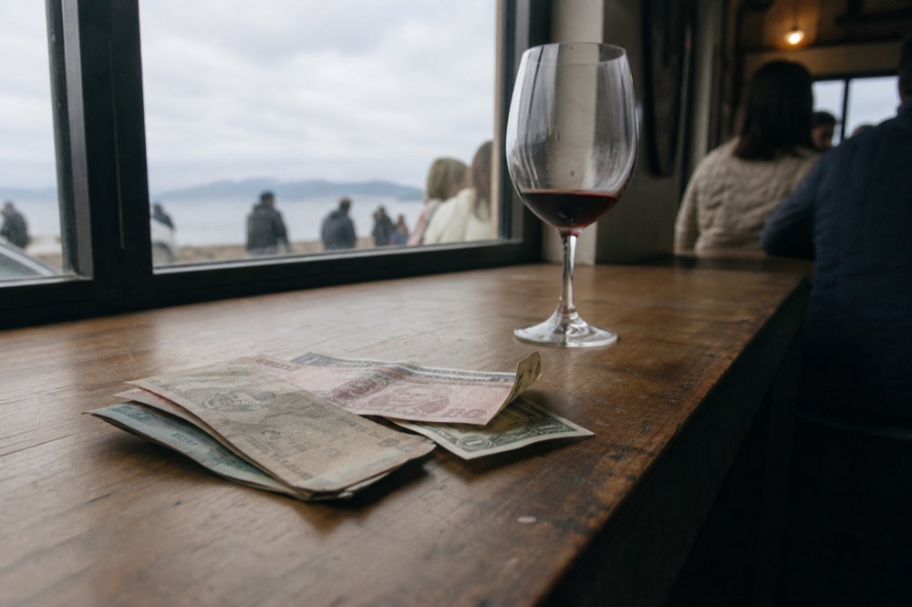 A stack of peso and dollar bills resting on a wooden tasting room counter, no text, no logos, no people