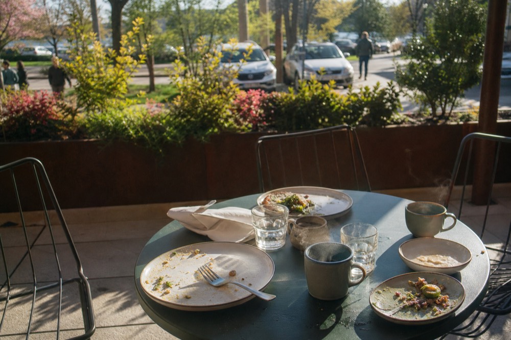 Shared dining table with brunch plates and coffee cups on a sunny patio, no text, no logos, no people
