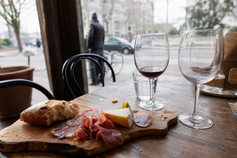 Charcuterie board with cured meats, cheese and bread on a wooden table beside wine glasses, no text, no logos, no people