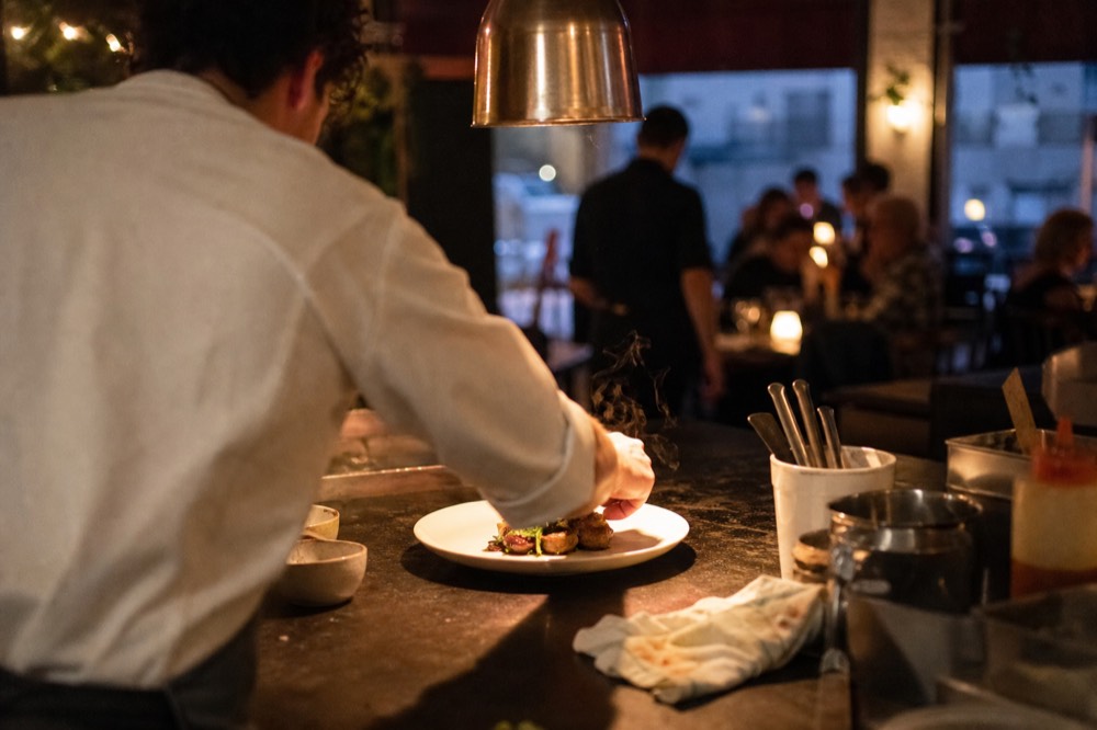 Chef plating a dish at a pass in an open kitchen, no text, no logos, no people