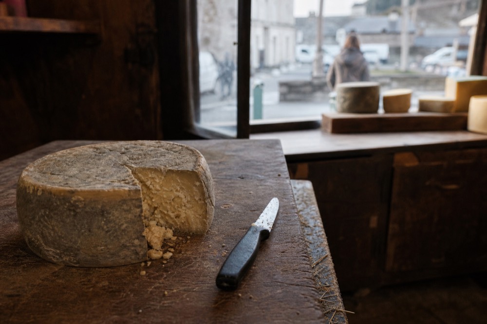 Wheel of aged cheese on a wooden counter in a small shop, no text, no logos, no people
