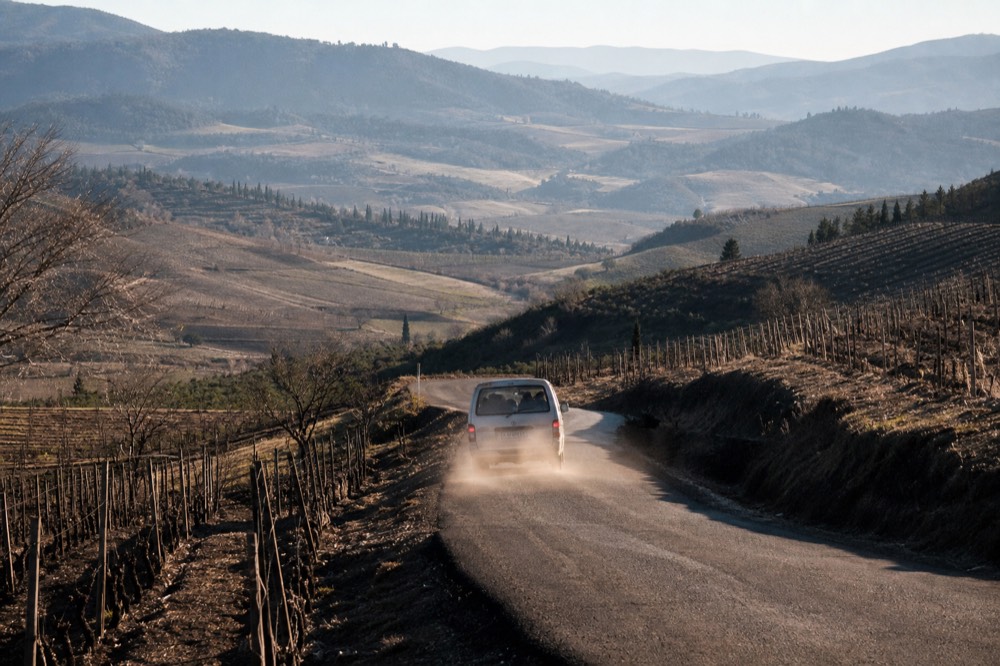 Tour vehicle driving a paved road through rolling Baja California wine country, no text, no logos, no people